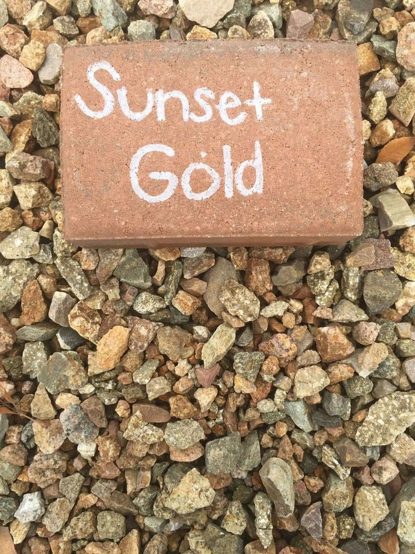 Brick labeled "Sunset Gold" lying on a bed of multicolored decorative gravel.